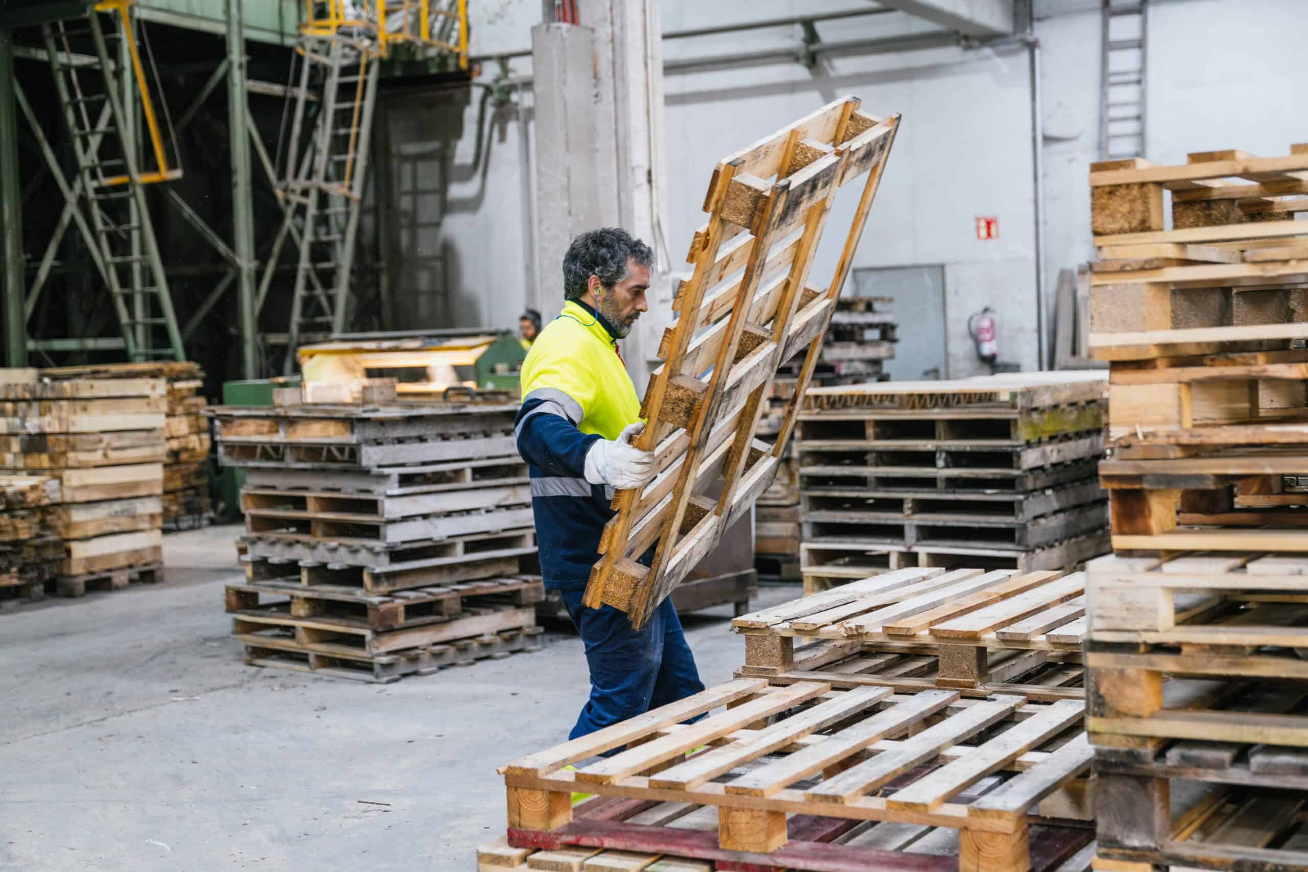 Factory worker carrying wooden pallet